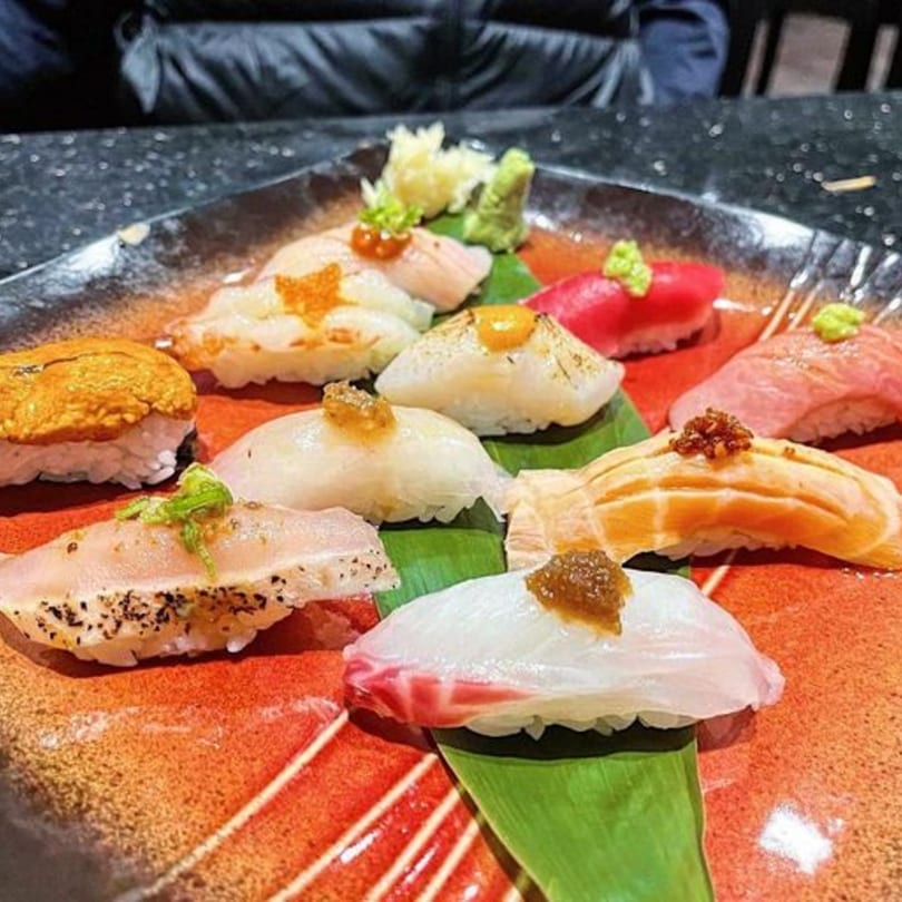 A vibrant platter of assorted nigiri sushi, including salmon, tuna, and whitefish, on a red plate.
