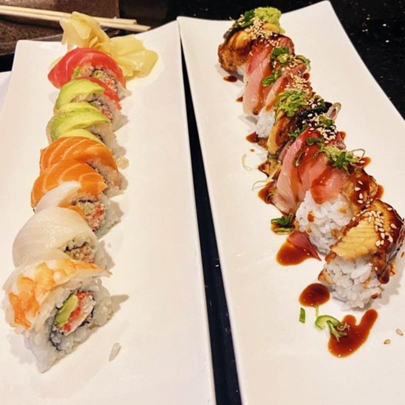 Two long plates of colorful sushi rolls, one with avocado and salmon, the other with eel and tuna.