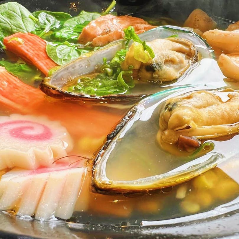 Close-up of a Japanese seafood soup with mussels, fish cakes, salmon, and spinach.