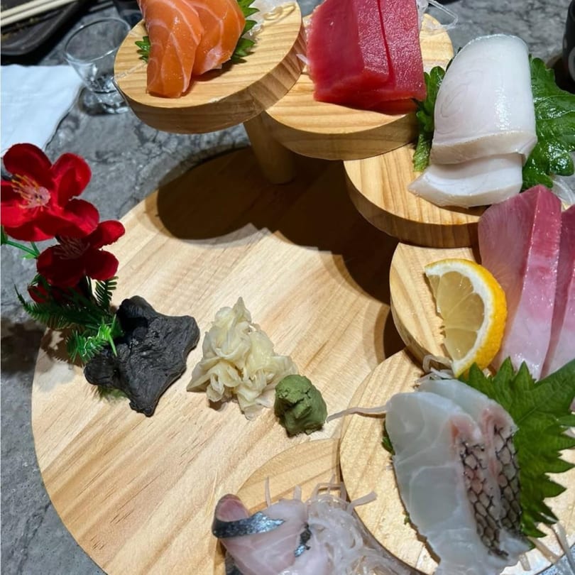 Assorted sashimi, including salmon, tuna, and white fish, artfully arranged on a tiered wooden platter.